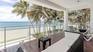 Un balcón con vista a la playa, palmeras y el océano.