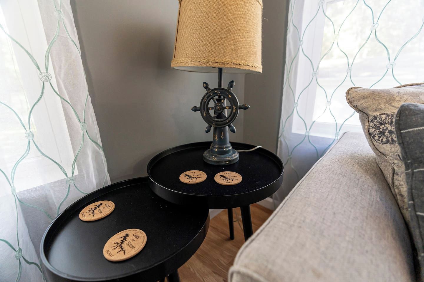 A corner of a room with a lamp on a small table, a cushion, and a wall with a patterned curtain.
