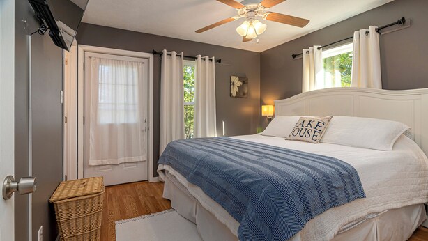 A bedroom with a large bed, a ceiling fan, a window with curtains, a wicker basket, and a white rug.