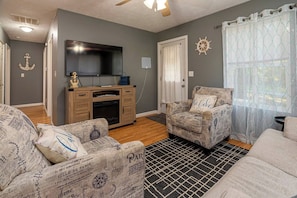 A living room with a flat-screen TV, wooden entertainment unit, patterned armchairs, and a black and white patterned rug. - Cozy, Pet Friendly Cottage near Lake of Egypt (Goreville)