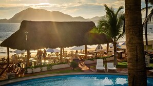 A pool area with lounge chairs and umbrellas, overlooking a body of water with mountains in the background. - Bungalows Casablanca Alamar (Manzanillo)