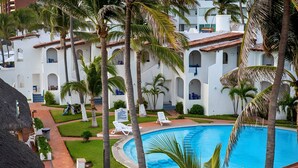 A pool area with lounge chairs and palm trees, surrounded by a building with multiple balconies. - Bungalows Casablanca Alamar (Manzanillo)