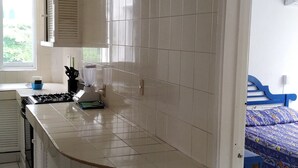 Egy praktikus, kis méretű konyha fehér csempékkel, beépített tűzhellyel és egy ablakkal, mely természetes fényt biztosít.