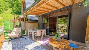 Una terraza de madera con suelo estampado, una silla colgante, una mesa con sillas y una planta en maceta.