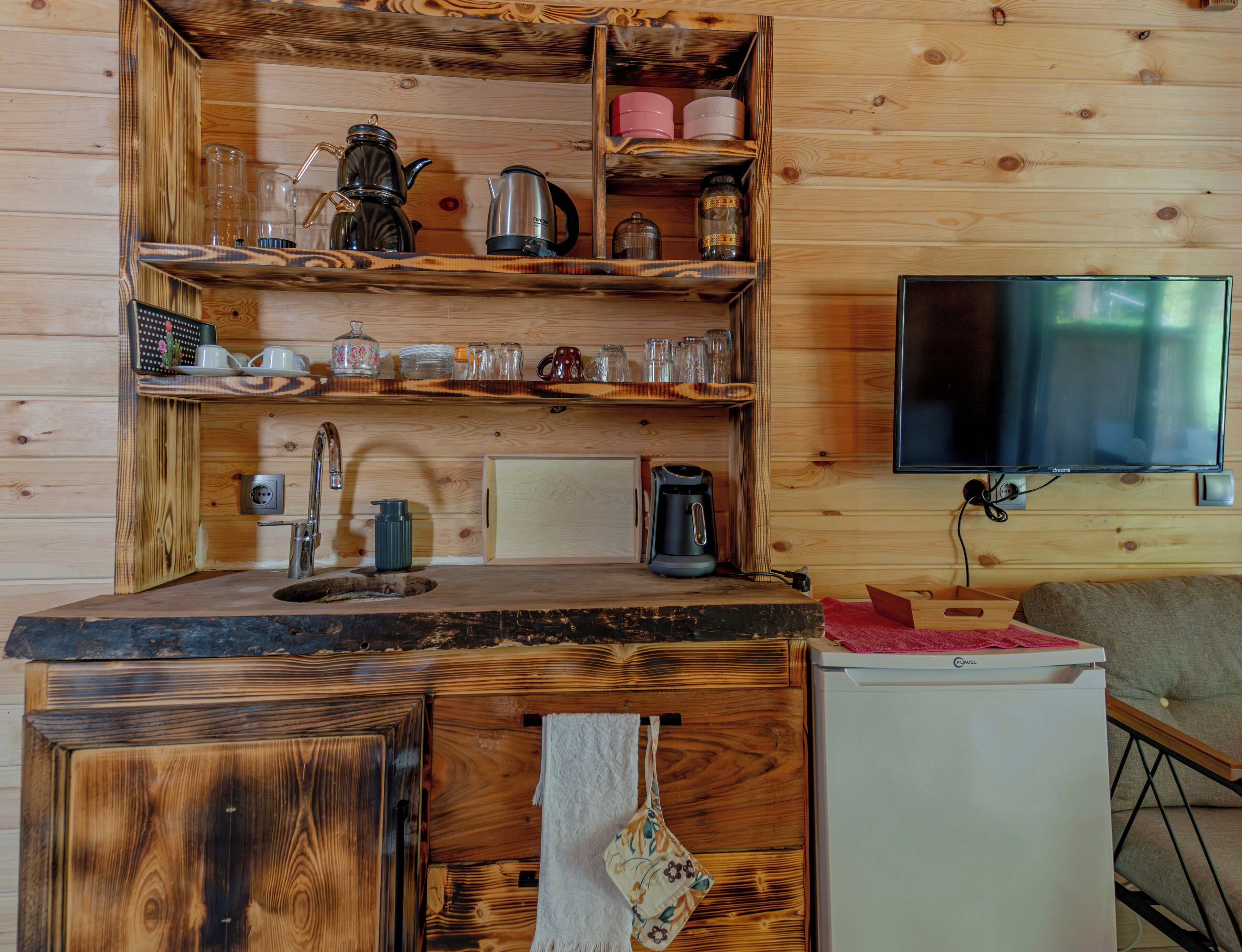 L’intérieur d’une cabane en bois comprend un espace cuisine équipé d’un évier, d’un plan de travail et d’un réfrigérateur.