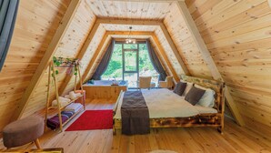 Un dormitorio acogedor en el ático con techo inclinado de madera, una cama, un pequeño rincón de descanso y vistas al exterior con vegetación.
