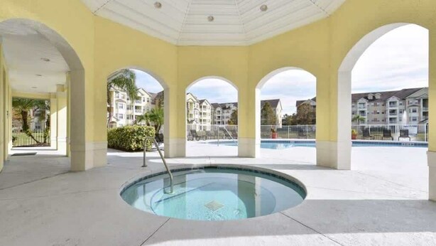 Un área de piscina cubierta con un jacuzzi central, rodeado de arcos y vistas a edificios residenciales.