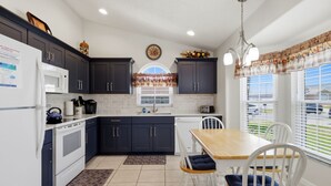 A kitchen with dark cabinets, a white refrigerator, a microwave, a stove, and a dining table with chairs.