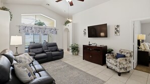 A living room with a ceiling fan, a sofa, a chair, a TV, and a window with a view.