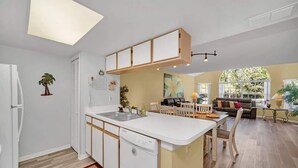 Une cuisine moderne avec un îlot central, un coin repas avec une table et des chaises, et un salon avec un canapé et une fenêtre.