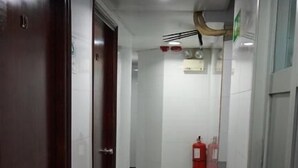 A corridor with wooden doors, white walls, a tiled floor, a ceiling light, and a fire extinguisher. - NEW MANDARIN GUEST HOUSE (Kowloon)