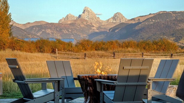 Een vuurkorftafel met vier Adirondack-stoelen gericht op een bergachtig landschap.