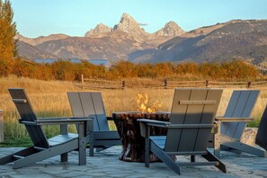Een vuurkorftafel met vier Adirondack-stoelen gericht op een bergachtig landschap.