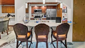 Cocina moderna con una isla central, armarios de madera, electrodomésticos de acero inoxidable y un comedor con sillas tapizadas.