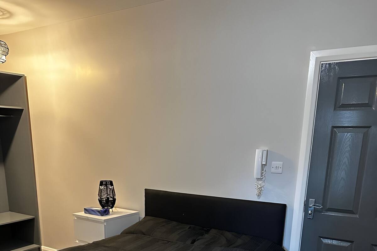 A neatly made bed with a dark headboard, a bedside table with a lamp, and a door to the right.