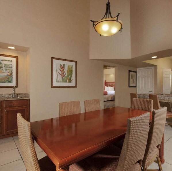 A dining area with a wooden table, wicker chairs, and a hanging light fixture. - Luxury Resort Minutes from Disney  (Kissimmee)