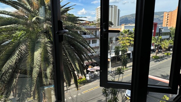 A view from a window overlooking a street with palm trees, a parked car, and buildings in the background. - Beautiful 3-bed 2-bath aptartment on la 70 with Air conditioning (Medellín)