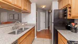 A kitchen with wooden cabinets, granite countertops, stainless steel appliances, and a hallway leading to another room. - Charming 2-bedroom, 2bath home in lovely Hammond (Hammond)