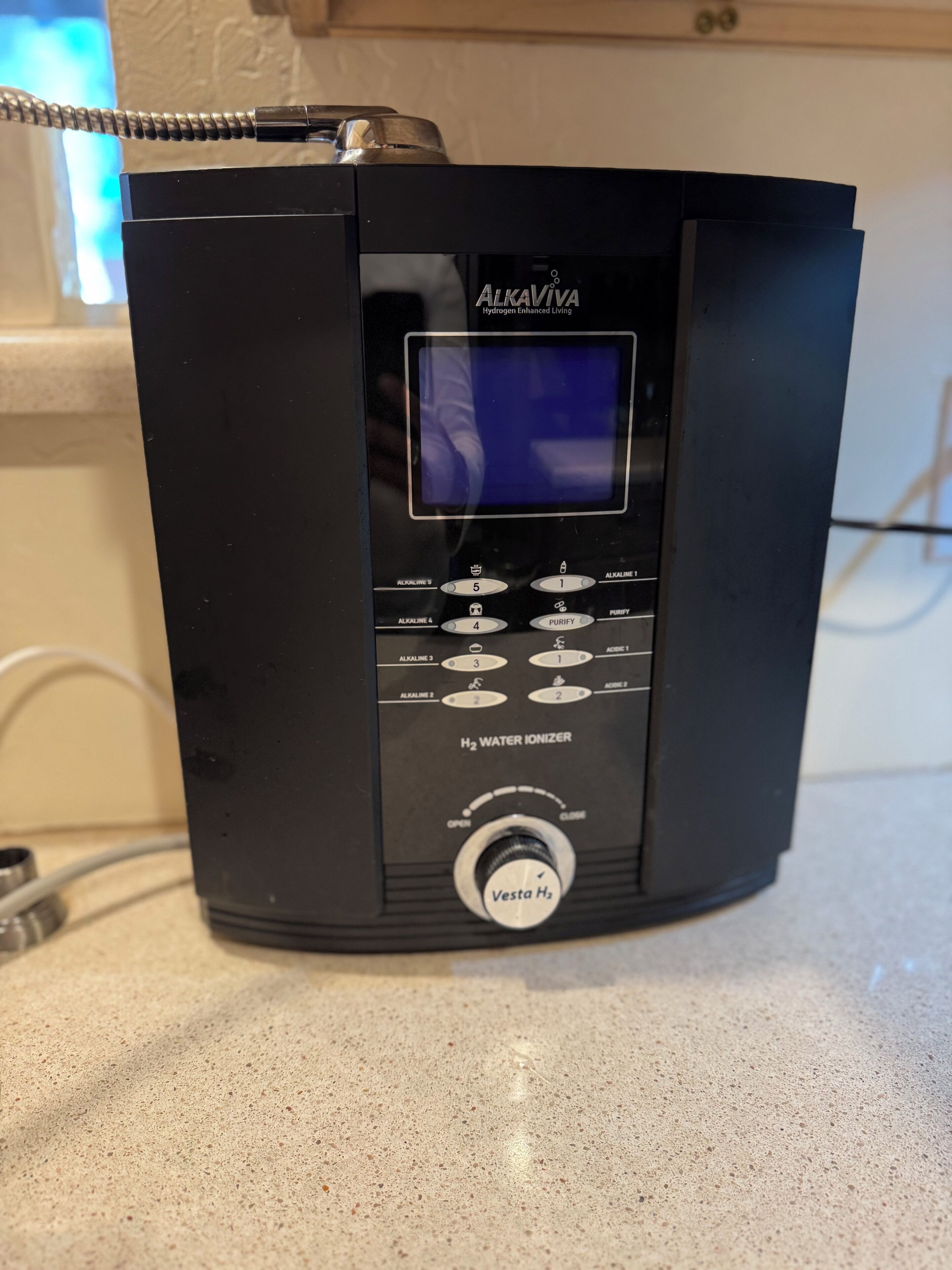 A black AlkaViva H2 water ionizer with a digital display, control buttons, and a knob labeled "Vesta H2".