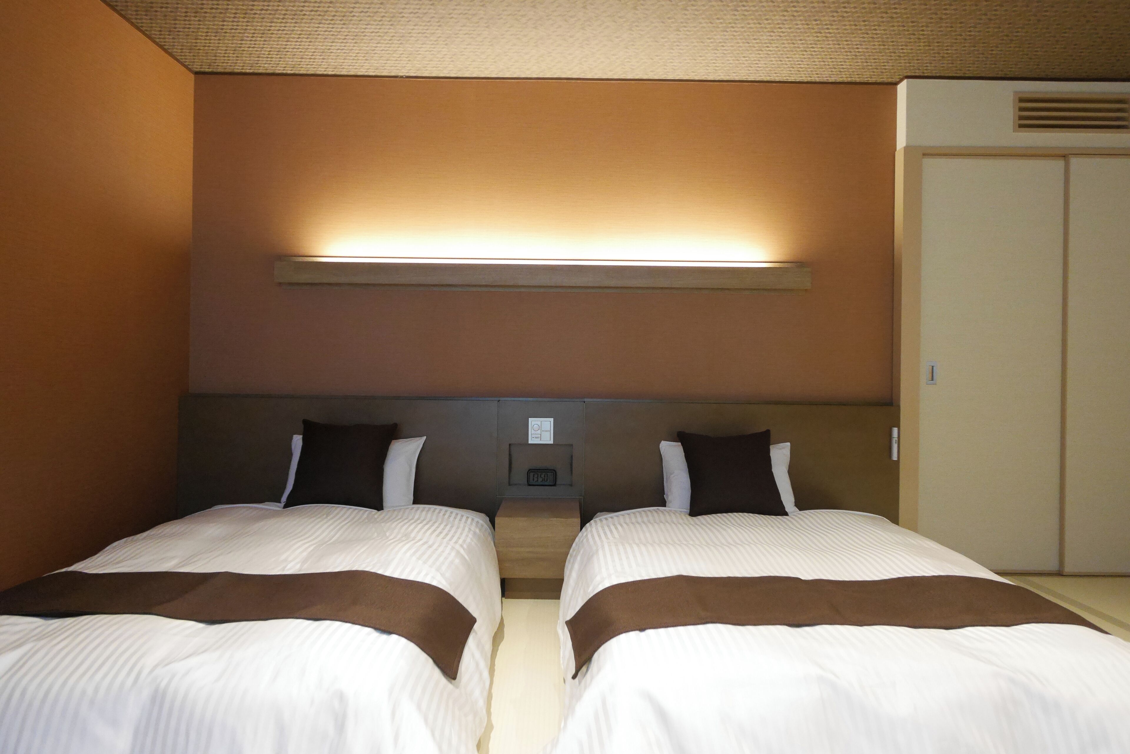 Una habitación de hotel con dos camas, una mesita de noche, una lámpara de pared y un armario.
