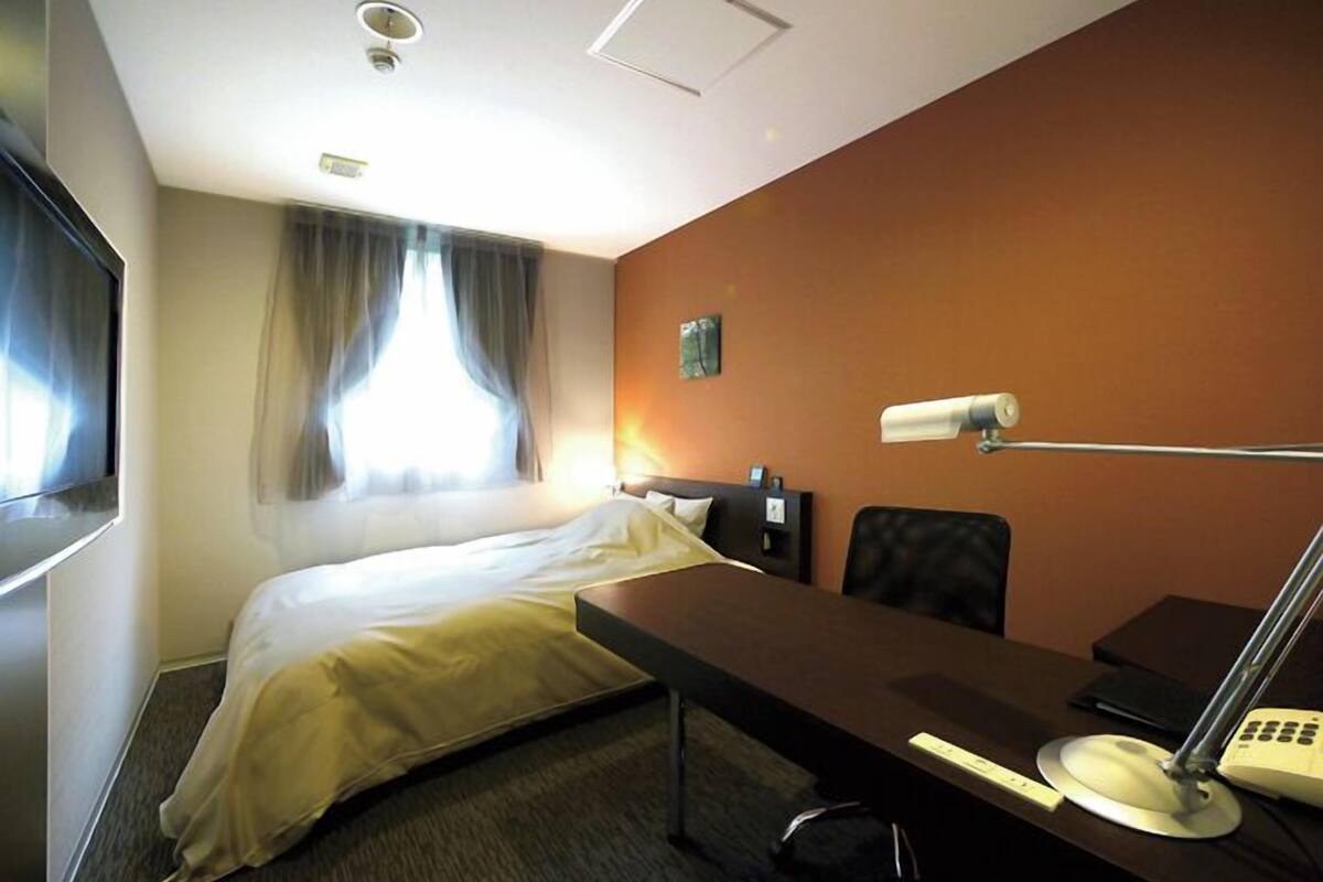 Een hotelkamer met een bed, een bureau, een stoel, een bureaulamp, een telefoon en een televisie.