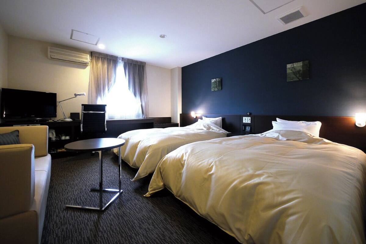 Een hotelkamer met twee bedden, een bureau, een stoel, een televisie en een raam met gordijnen.