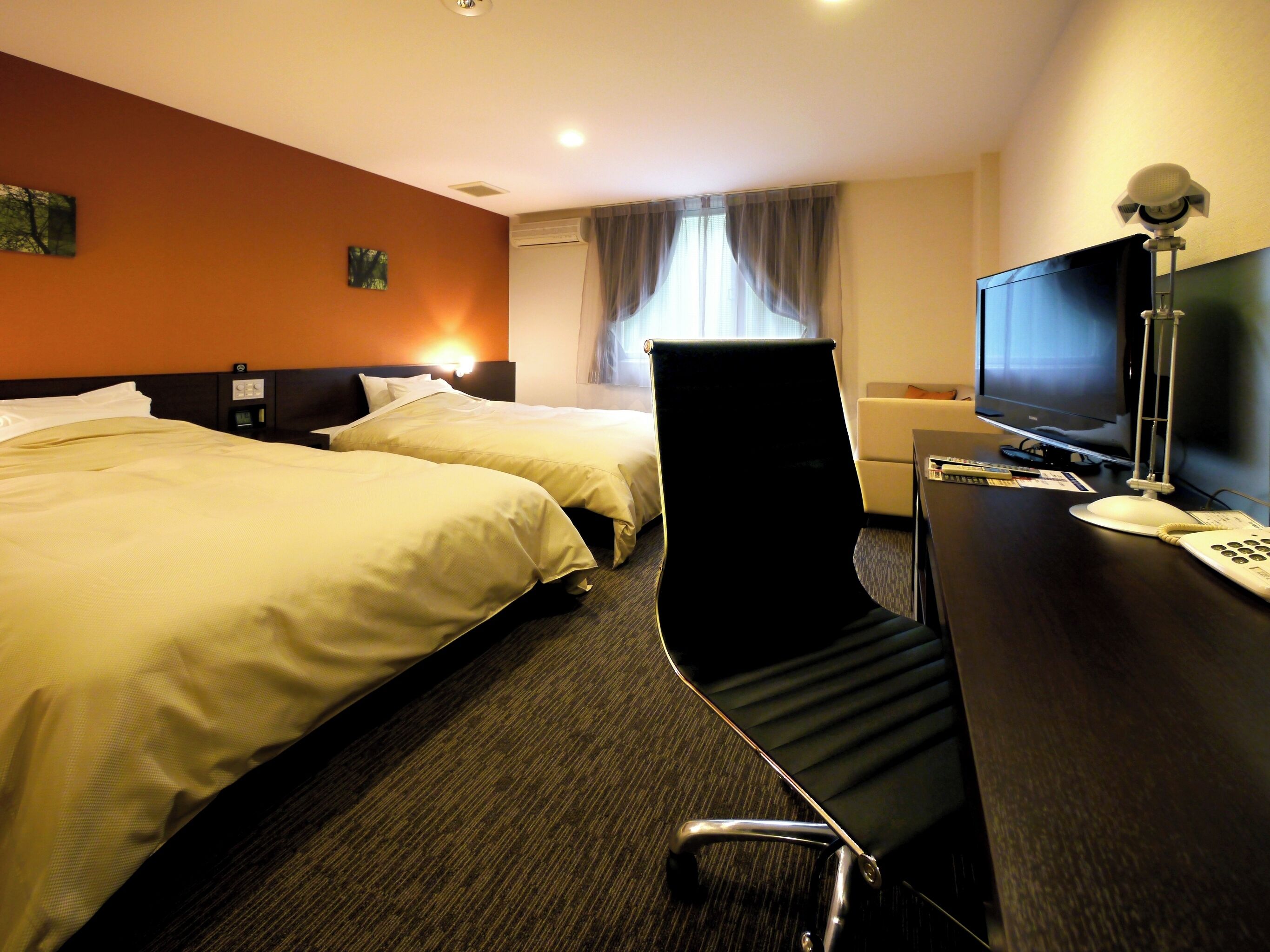 Ein Hotelzimmer mit zwei Betten, einem Schreibtisch mit Computer und Telefon sowie einem Fernseher.