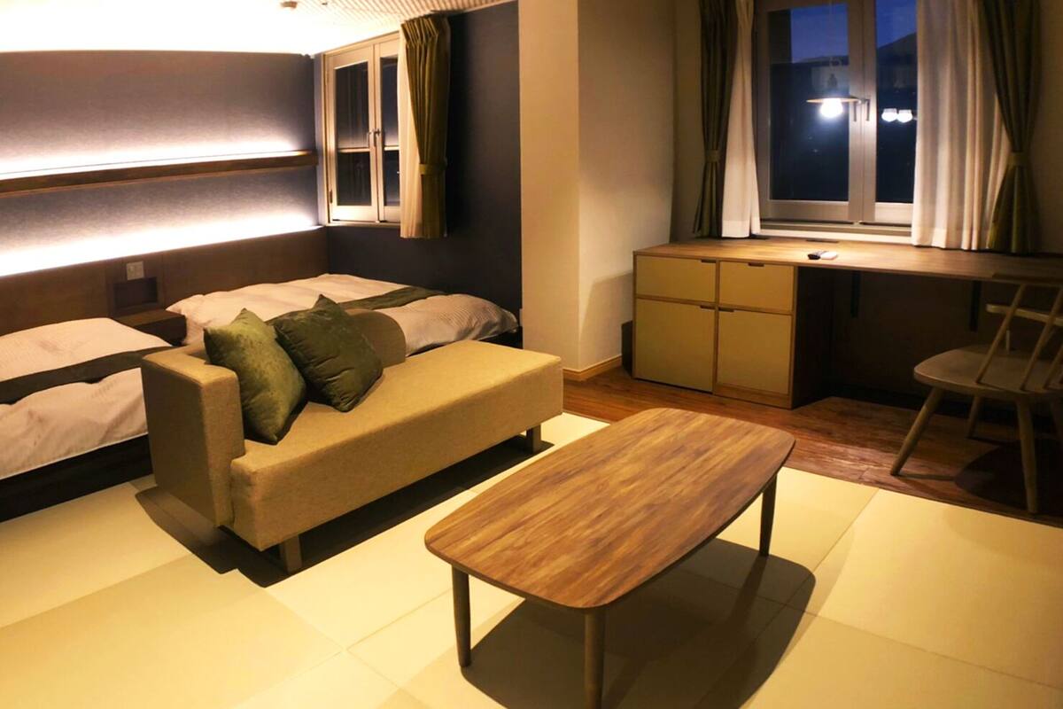 Een knus hotelkamer met een slaapbank, een klein houten tafeltje en een bureau met stoel.