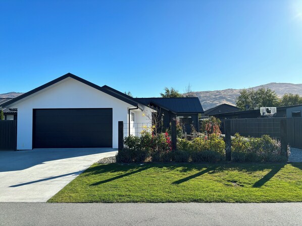 A modern two-story house with a large garage, a well-maintained lawn, and a mountain backdrop.