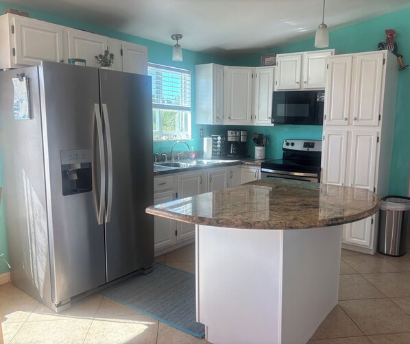 A kitchen with white cabinets, a stainless steel refrigerator, a granite countertop, a microwave, and a stove.
