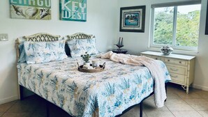 Un dormitorio con cama, mesita de noche, ventana y cuadros en las paredes.