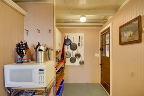 A compact kitchen with a microwave, utensils, and a pegboard with pots and pans.
