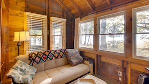 A cozy cabin interior with a sofa, a lamp, and large windows. - Rustic Cliff-top Cabin at the Tip of Lake Champlain's Barney Point (Colchester)