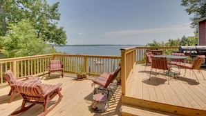 A wooden deck with outdoor furniture, including rocking chairs and a table with chairs, overlooking a body of water. - Rustic Cliff-top Cabin at the Tip of Lake Champlain's Barney Point (Colchester)