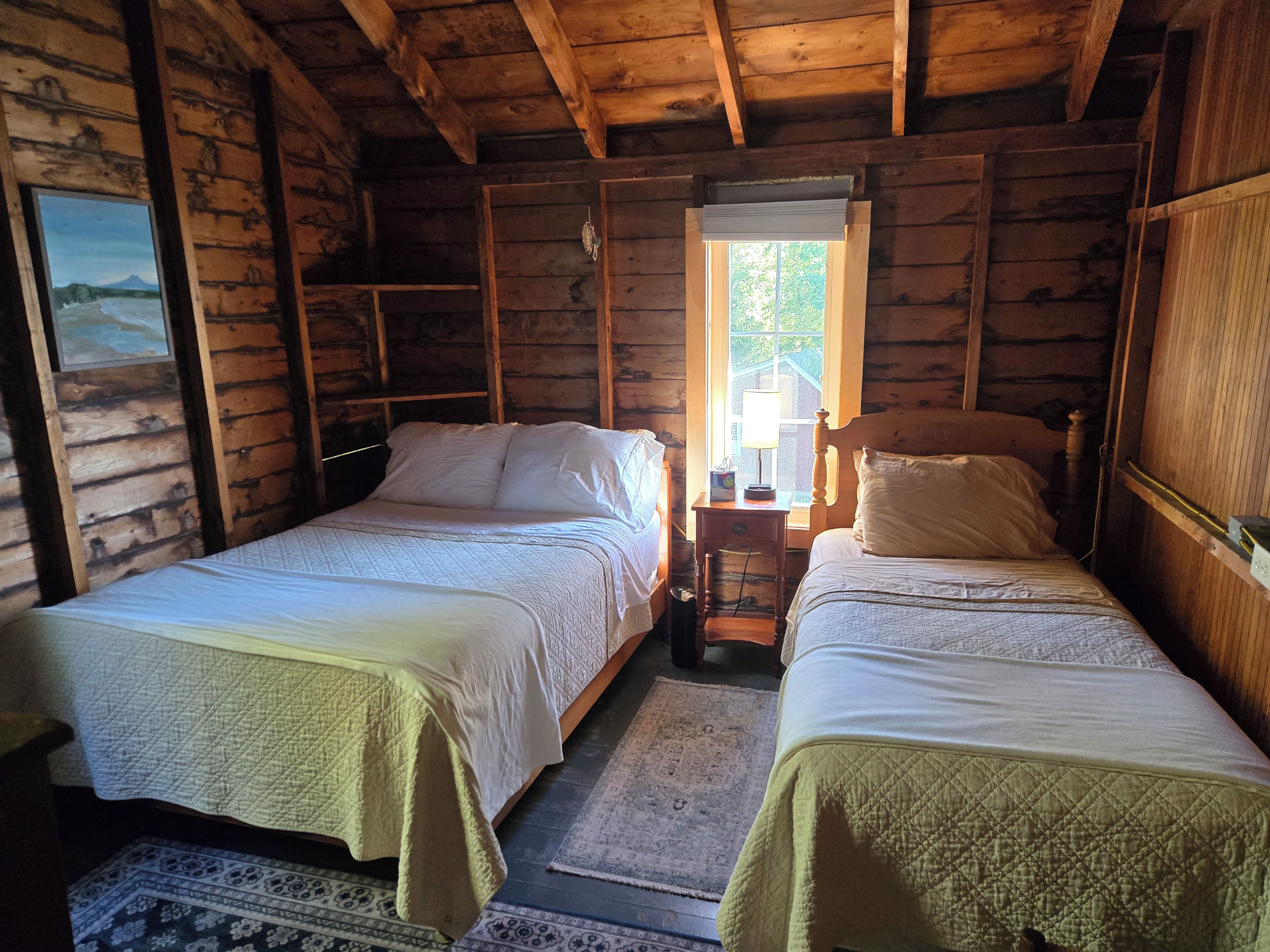 A cabin with two beds, a window with a view, and a wooden ceiling.
