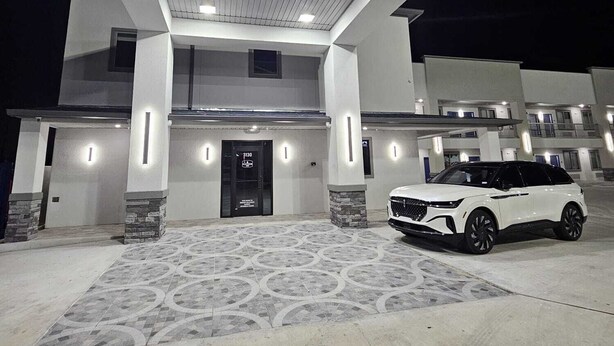 A modern building with a large entrance, a white car parked in front, and a patterned floor. - Platinum inn (Katy)