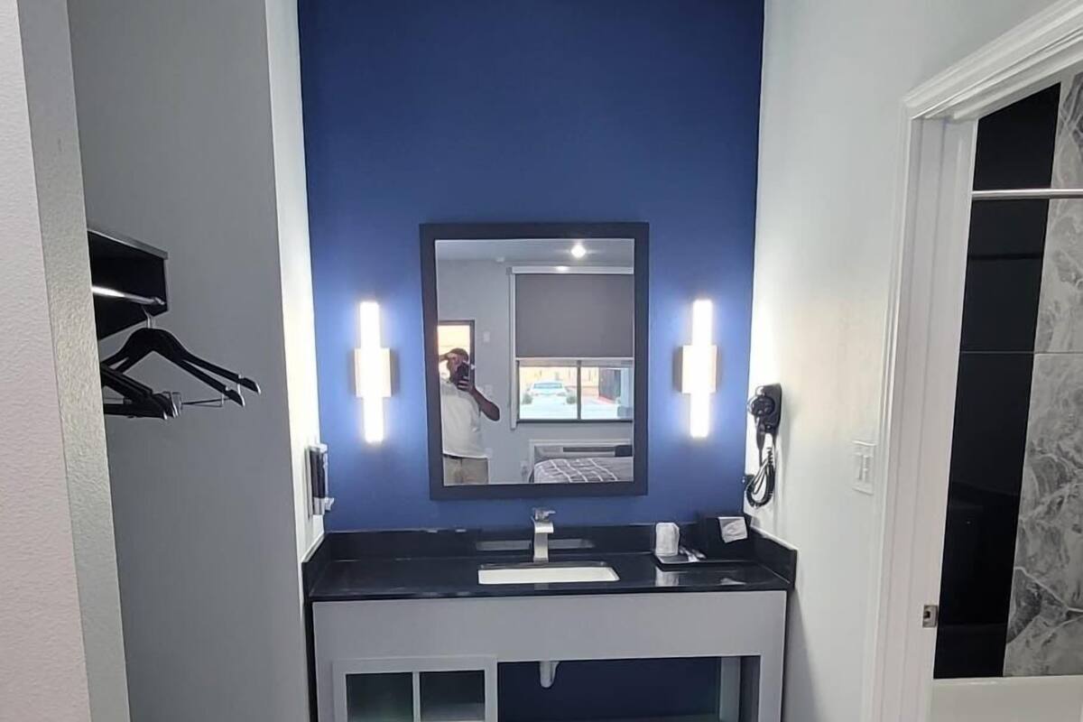 A bathroom with a dark blue accent wall, a large mirror, and a vanity with two sinks.