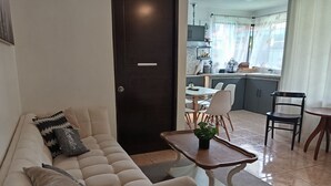 A living room with a sofa, a small table, and a potted plant. There is a dining area with chairs and a table in the background. - Your-Holiday home fortuna arenal with swimming pool (La Fortuna)