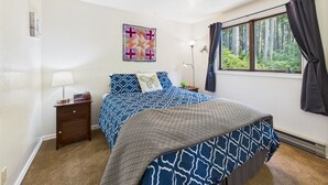 Una camera da letto con un letto, un comodino, una lampada, una finestra con tende e un quadro appeso al muro.