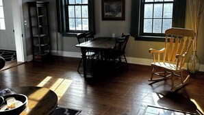 Un espace repas comprenant une table et des chaises en bois, un lustre et de grandes fenêtres avec des rideaux.