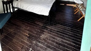 Une chambre avec un lit, un bureau et une chaise. Il y a des fenêtres avec des rideaux, un ventilateur de plafond et un plancher en bois.