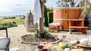 A patio with a hot tub, a wooden table with food and drinks, and a chair.