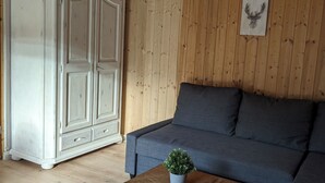 A wooden-paneled room with a white armoire, a blue sofa, and a wooden coffee table with a plant. - Vacation home with outdoor sauna in the Thuringian Forest (Schleusegrund)