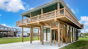 A two-story wooden structure with a balcony, a covered area, and a concrete foundation. - 3 Bdr/3 Bth, King Bed, No Fees (Bolivar Peninsula)