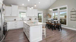 A spacious kitchen with white cabinets, a large island, and a dining area with wooden chairs. - 3 Bdr/3 Bth, King Bed, No Fees (Bolivar Peninsula)