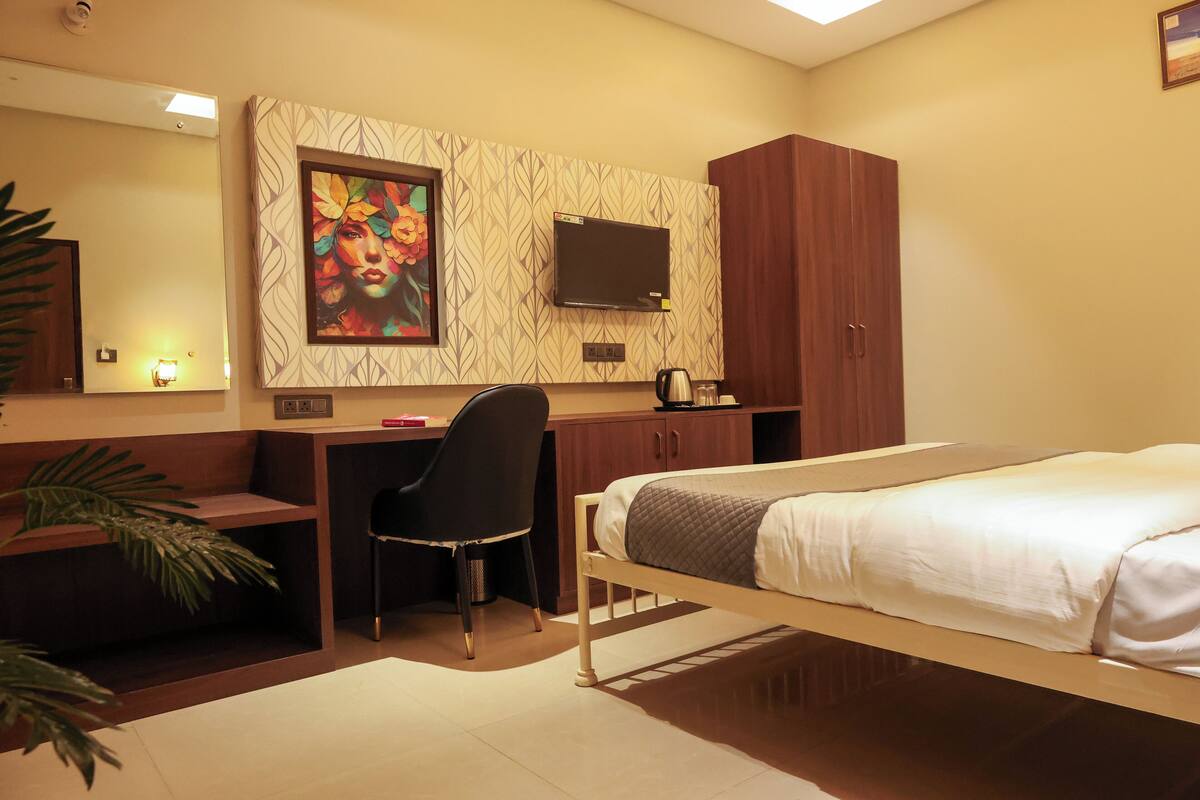 Une chambre d’hôtel équipée d’un lit, d’un bureau, d’une chaise, d’une télévision, d’une armoire et d’un tableau accroché au mur.