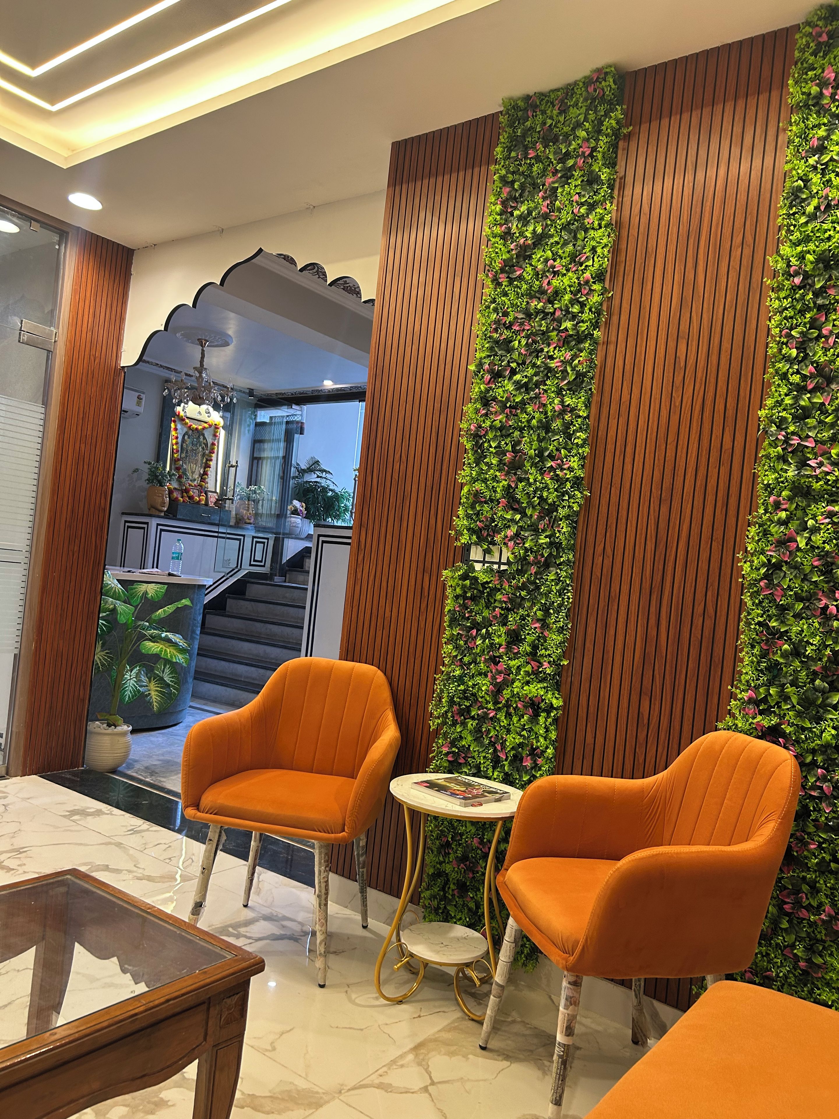 Un interior moderno con dos sillones naranjas, una mesa redonda pequeña, un espejo decorativo y una pared jardín vertical.