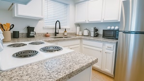 A modern kitchen with white cabinets, a granite countertop, a stainless steel refrigerator, and a built-in microwave.