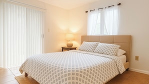 A bedroom with a bed, a nightstand, a lamp, and a window with curtains.