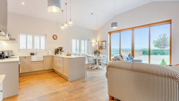 Una cocina amplia con una isla central, un comedor con sillas blancas y un ventanal con vistas al exterior.